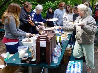 People gathering around a table at a Sierra Roots community meal outdoors.